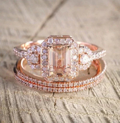Rose gold ring with emerald-cut center stone and diamond accents on a textured surface