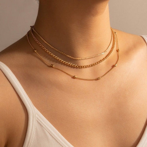 Close-up of a person wearing multiple gold necklaces on a neutral background