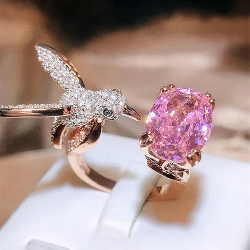 Rose gold ring with pink gemstone and intricate design on a white surface