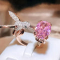 Rose gold ring with pink gemstone and intricate design on a white surface