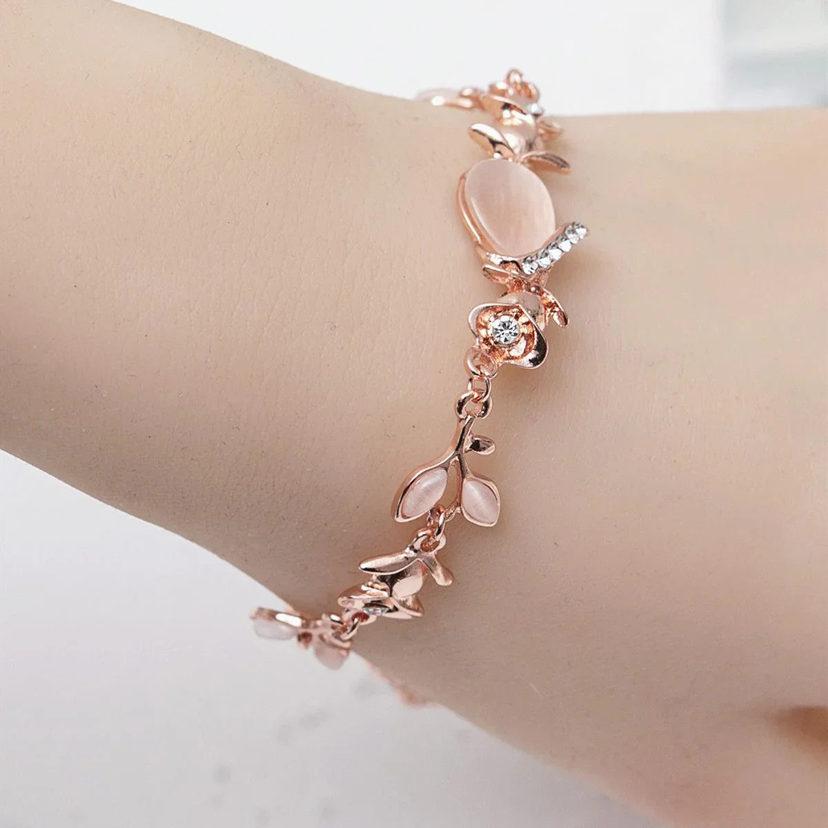 Rose gold bracelet with floral designs on a wrist against a white background
