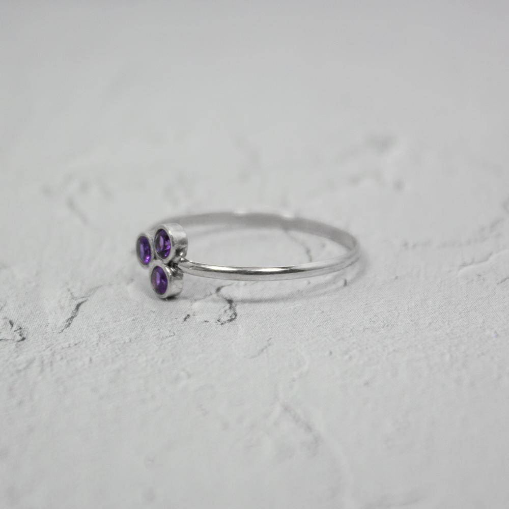 Silver ring with purple gemstone laying on light grey textured surface 